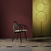 Beige chair with black accents, set against a burgundy wall and yellow backdrop, on a patterned geometric rug.