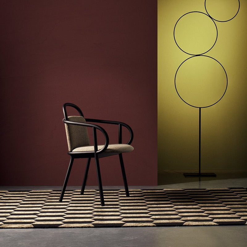 Beige chair with black accents, set against a burgundy wall and yellow backdrop, on a patterned geometric rug.