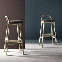 "Modern bar stools with a soft gray seat and light beige frame, featuring a minimalist design against contrasting dark walls."