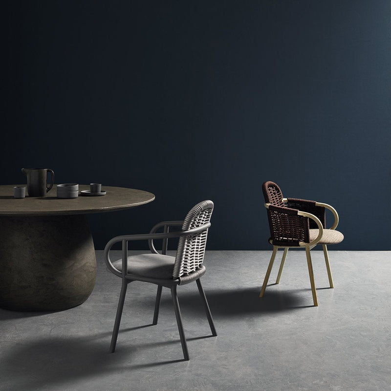 Modern chairs in gray and brown wicker with a minimalist round table against a dark blue wall. Stylish design elements.