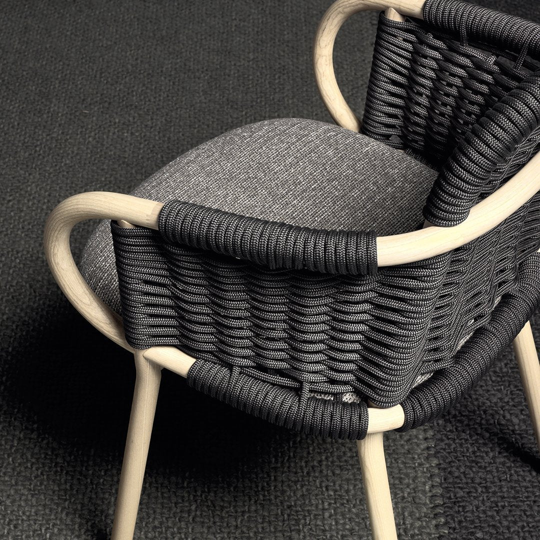 Black woven chair with gray cushion, featuring natural wood accents and a textured pattern on the seat.