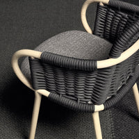 Black woven chair with gray cushion, featuring natural wood accents and a textured pattern on the seat.