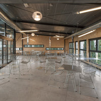 Stylish clear acrylic chairs and tables in a modern, open-space setting with neutral tones and industrial accents.