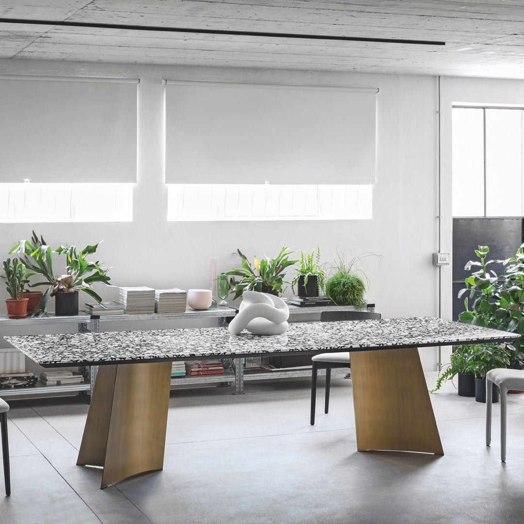 Stylish black and white speckled tabletop with gold geometric legs, surrounded by greenery in a modern interior.