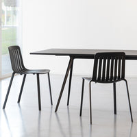 Black dining table and chairs with sleek lines and a minimalist design on a light gray floor. Modern aesthetic.