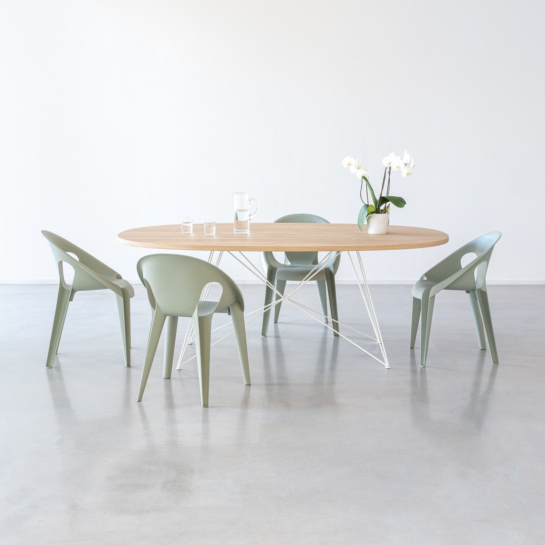 Light wood table with rounded edges, four soft green chairs, and a white backdrop for a fresh, modern look.