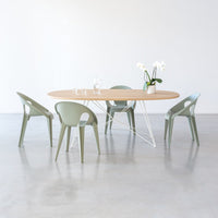 Light wood table with rounded edges, four soft green chairs, and a white backdrop for a fresh, modern look.