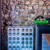 White bottle rack with green dish tray against a textured stone wall. Clear and vibrant color contrast.