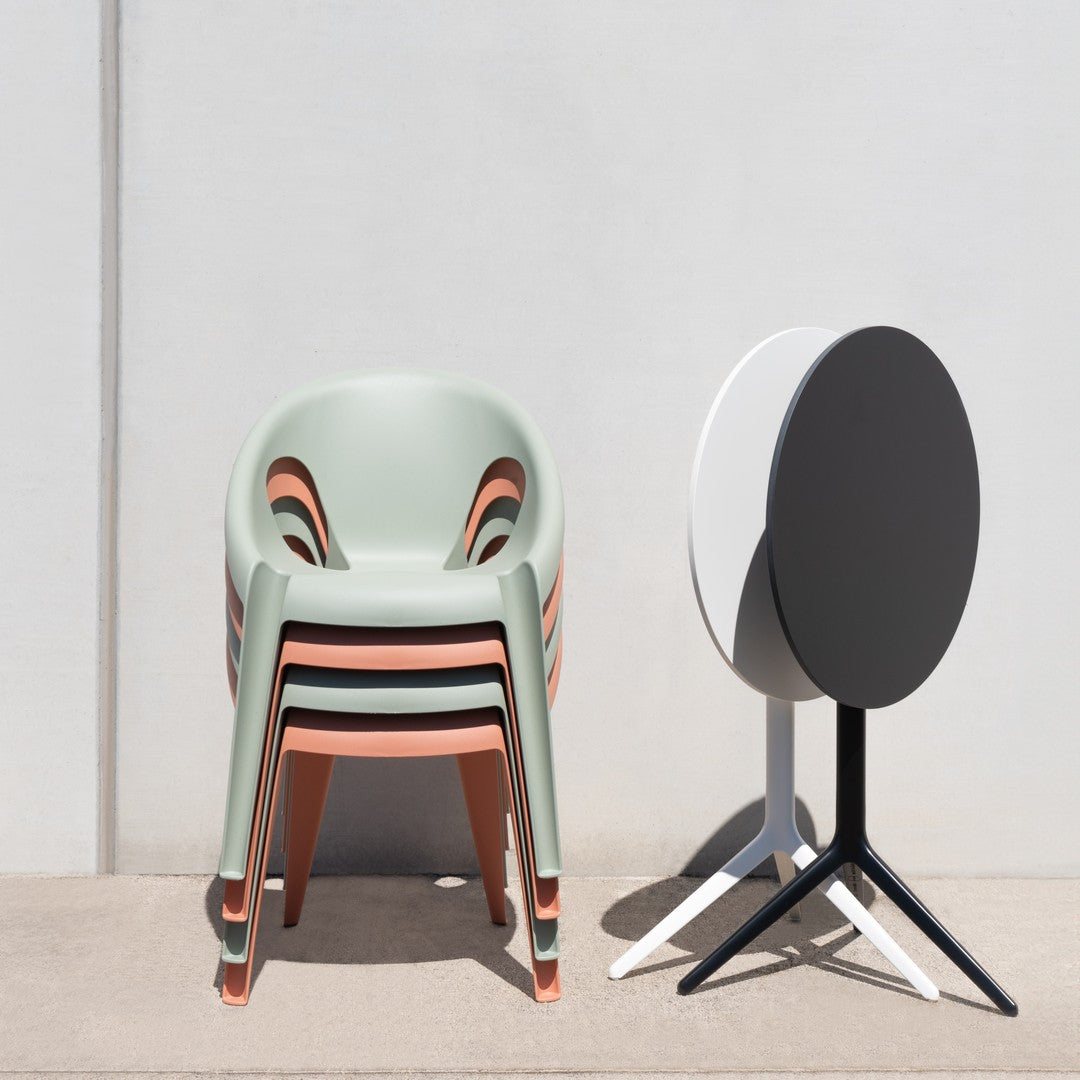 Stacked chairs in soft green, peach, and gray, paired with a round black and white table against a neutral background.