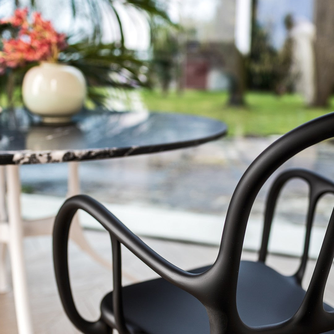 Black curved chair with a sleek matte finish, paired with a round black marble table featuring white veining.