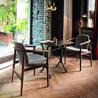 Gray upholstered chairs with a dark wood frame, paired with a black metal table on a herringbone-pattern wooden floor.