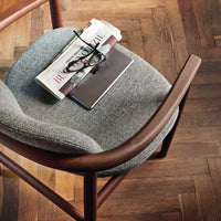 Gray textured upholstery on a wooden chair with rich brown tones, complemented by a herringbone-patterned floor.