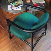 Modern black armchair with a plush emerald green seat, set against a wooden floor and vibrant decor.