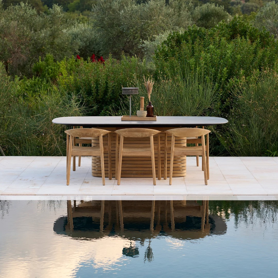 Modern outdoor dining table in natural wood with sleek dark tabletop, surrounded by light wooden chairs and lush greenery.