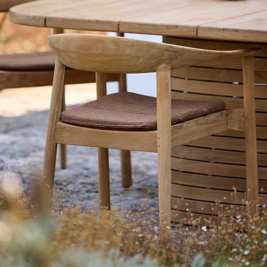 Natural wood chair with a light finish and a dark brown seat cushion, set against a neutral outdoor backdrop.