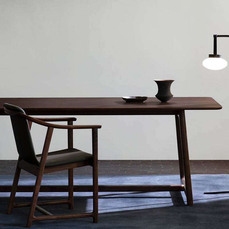 Elegant dark wood dining table with minimalist black chair and muted tone decor against a light gray wall.
