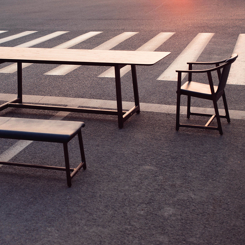 Modern black table and bench with simple lines, set against a faded asphalt background and subtle sunset hues.
