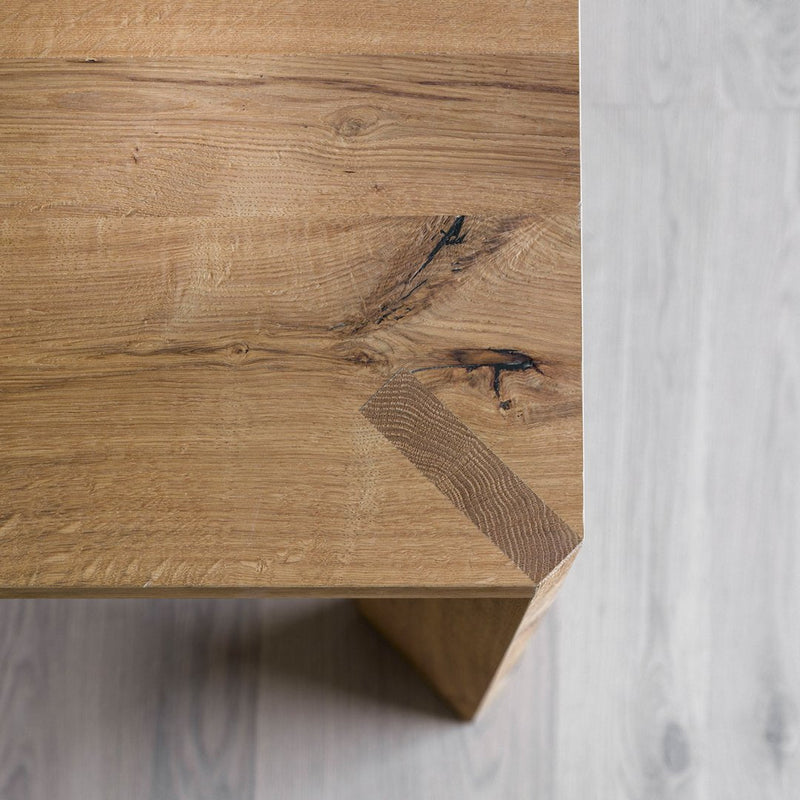 Natural wood table with a warm oak finish, featuring unique grain patterns and knots on a light wood floor.