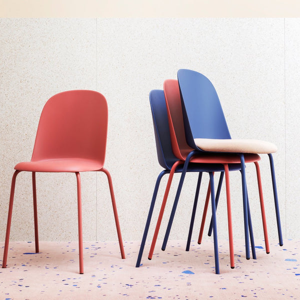 Colorful stackable chairs in pink, blue, and cream with sleek metal legs against a speckled pastel background.