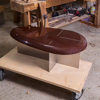Sleek maroon glossy coffee table with a shiny silver geometric base on a wooden cart. Modern design, minimalist style.