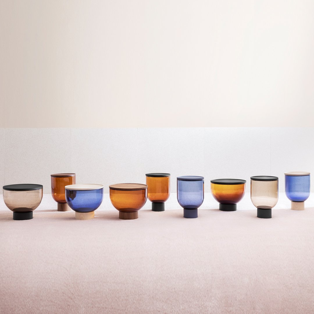 Colorful glass cups in amber, blue, and beige with unique patterns and a modern design displayed on a soft pink background.