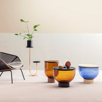 Amber and blue glass vases with sleek black bases, set against a minimalist beige and gray background.