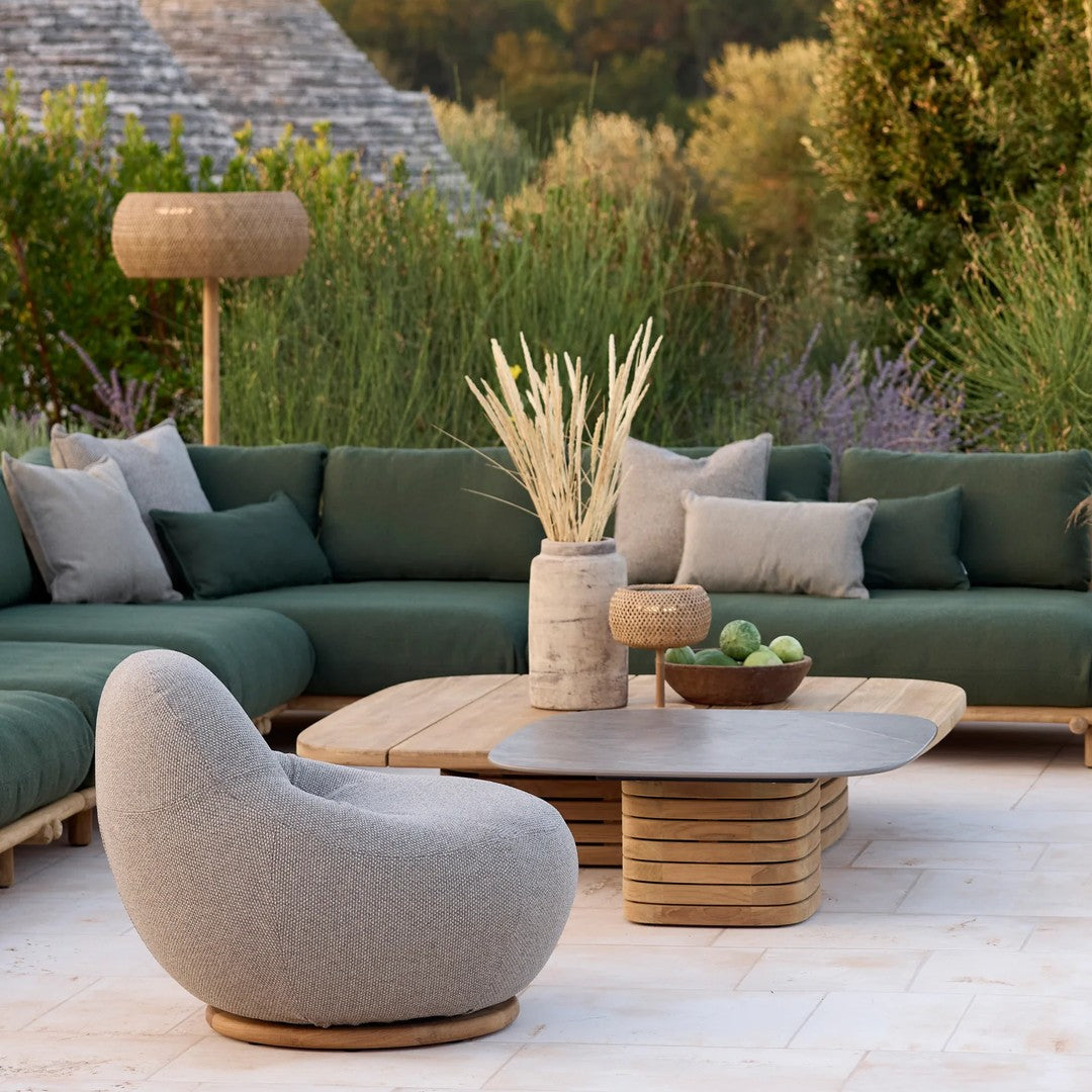 Modern outdoor seating set featuring deep green cushions, soft gray chair, and natural wood accents on a light stone patio.