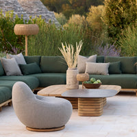 Modern outdoor seating set featuring deep green cushions, soft gray chair, and natural wood accents on a light stone patio.