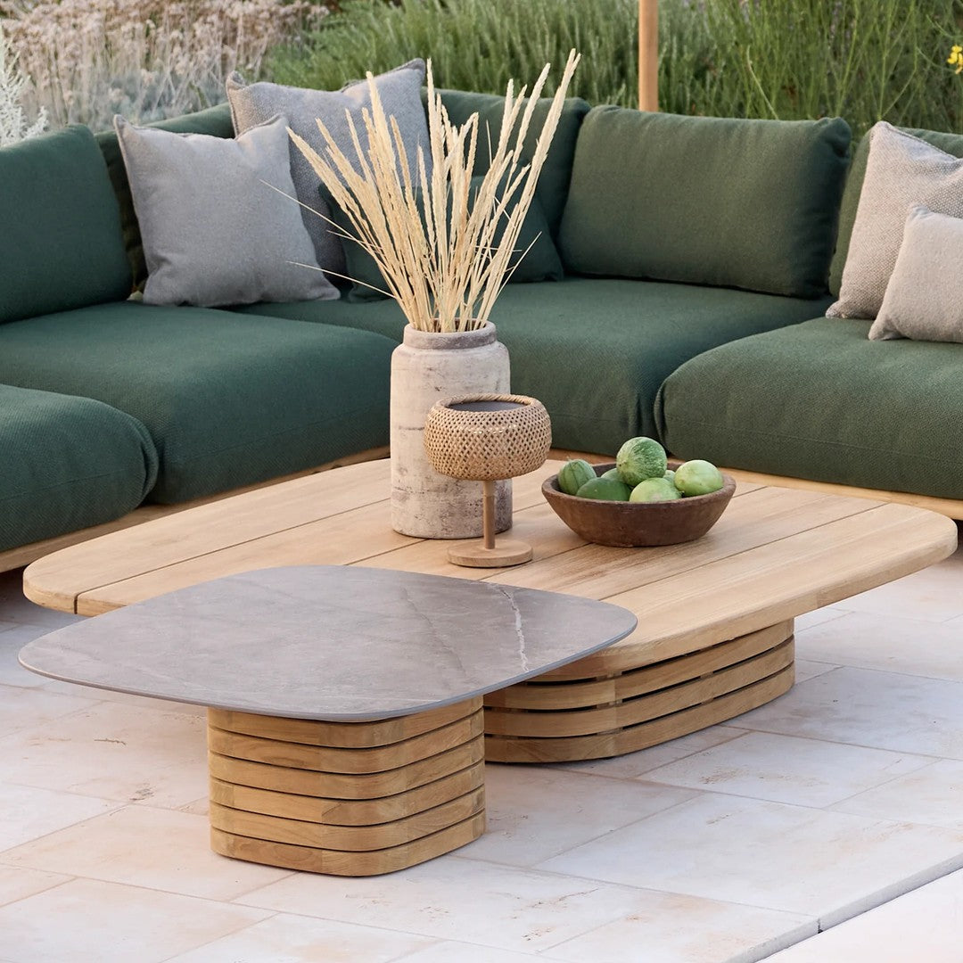 Wooden coffee table with a smooth gray top, surrounded by green cushions and neutral-toned decor elements.