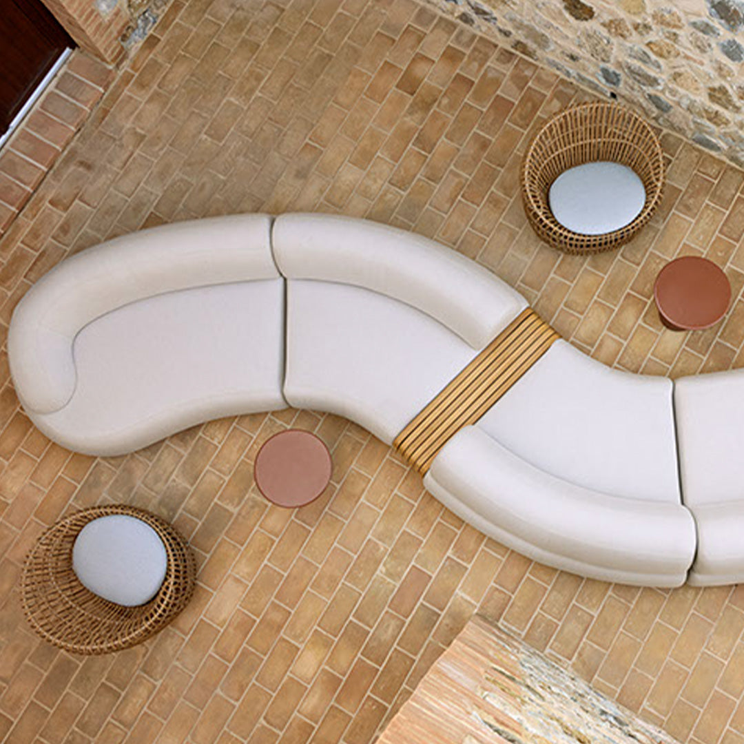 Curved beige sofa with bamboo accents, complemented by round terracotta and mirrored tables on a textured stone floor.