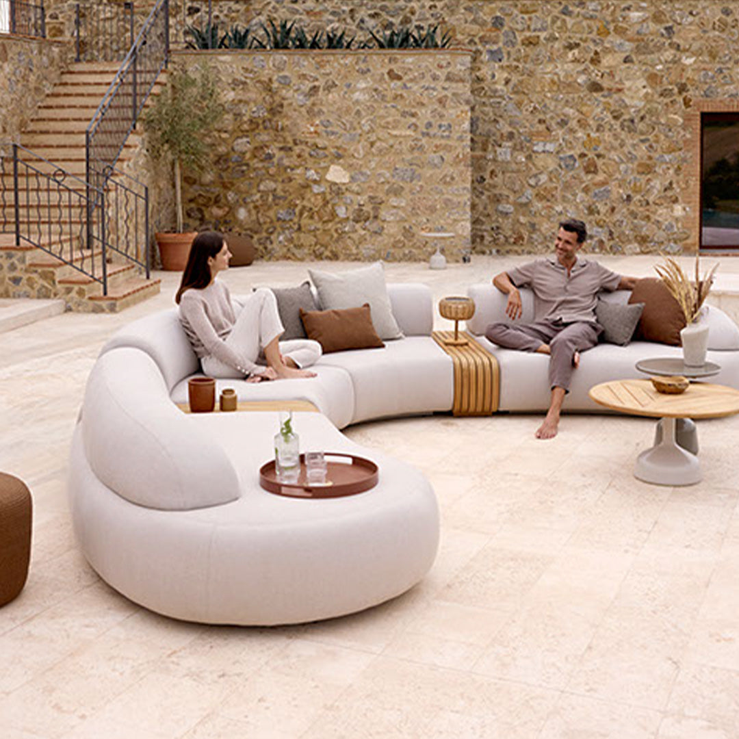 Curved beige sofa with brown accent pillows, set against a rustic stone backdrop.