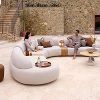 Curved beige sofa with brown accent pillows, set against a rustic stone backdrop.