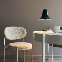 Textured cream chair and glossy green lamp on a minimalist white table against a soft gray wall.