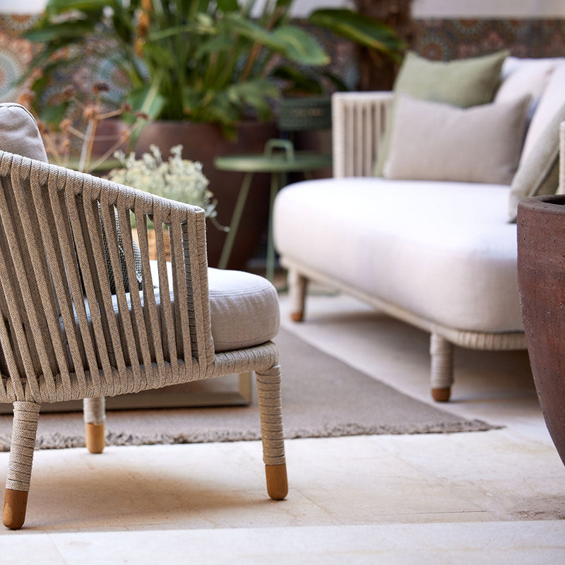 Neutral beige and taupe outdoor furniture with textured patterns, complemented by green cushions and lush greenery.
