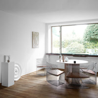 Minimalist dining set featuring clear wire chairs and wooden accents, set against a bright, airy, white background.