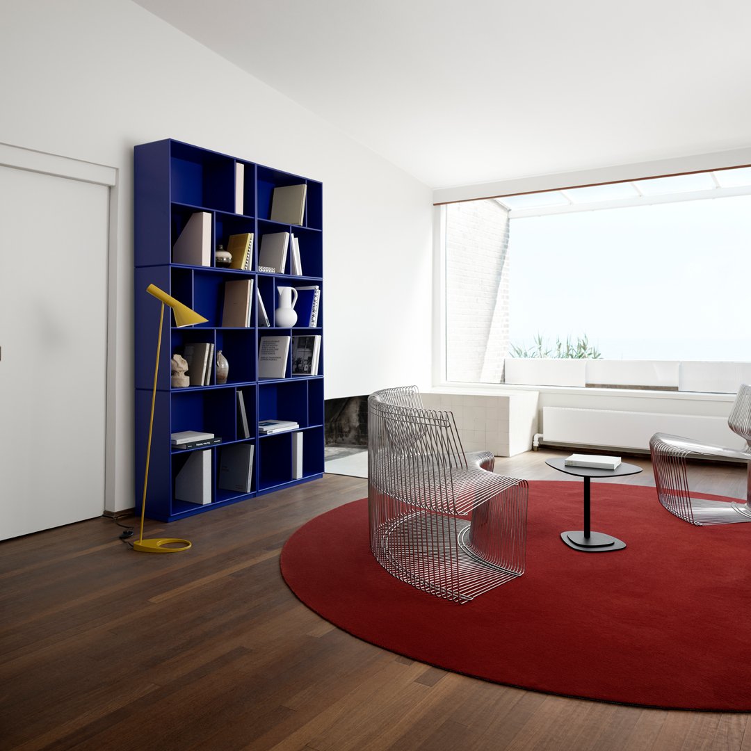Vibrant blue bookshelf, sleek clear chairs, oversized red circular rug, and warm wood flooring in a modern setting.