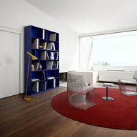 Vibrant blue bookshelf, sleek clear chairs, oversized red circular rug, and warm wood flooring in a modern setting.