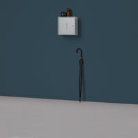 Gray wall-mounted box and black umbrella against a deep blue wall, featuring a smooth gray floor for contrast.