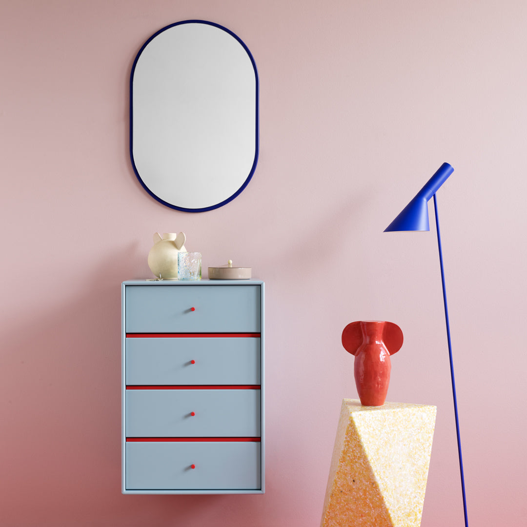 Stylish blue chest of drawers with red accents against a pink wall, complemented by a blue lamp and colorful decor.