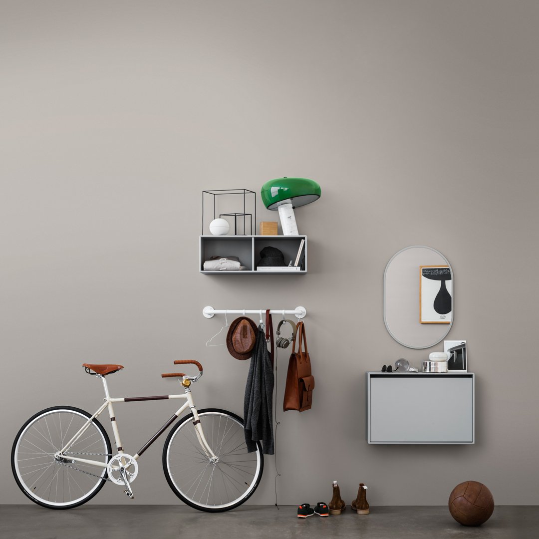 Modern storage and decor: green lamp, neutral wall, white bike, brown accents, grey shelf, and black accessories.