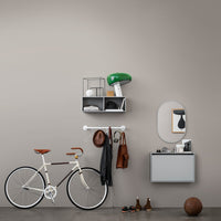 Modern storage and decor: green lamp, neutral wall, white bike, brown accents, grey shelf, and black accessories.
