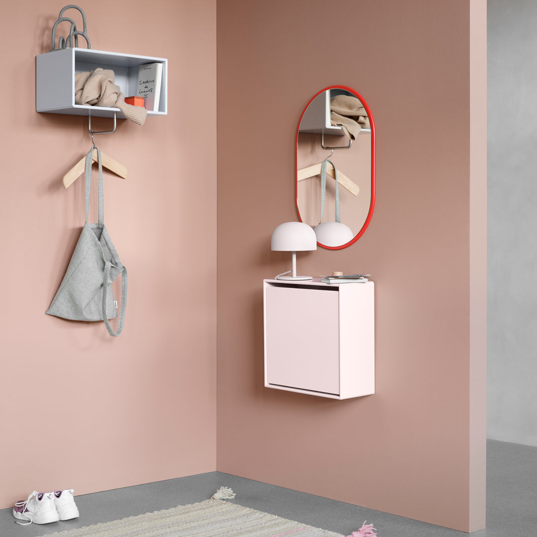 Soft pink wall with a light gray shelf and a red-framed mirror. Gray bag and pastel rug add subtle texture to the space.