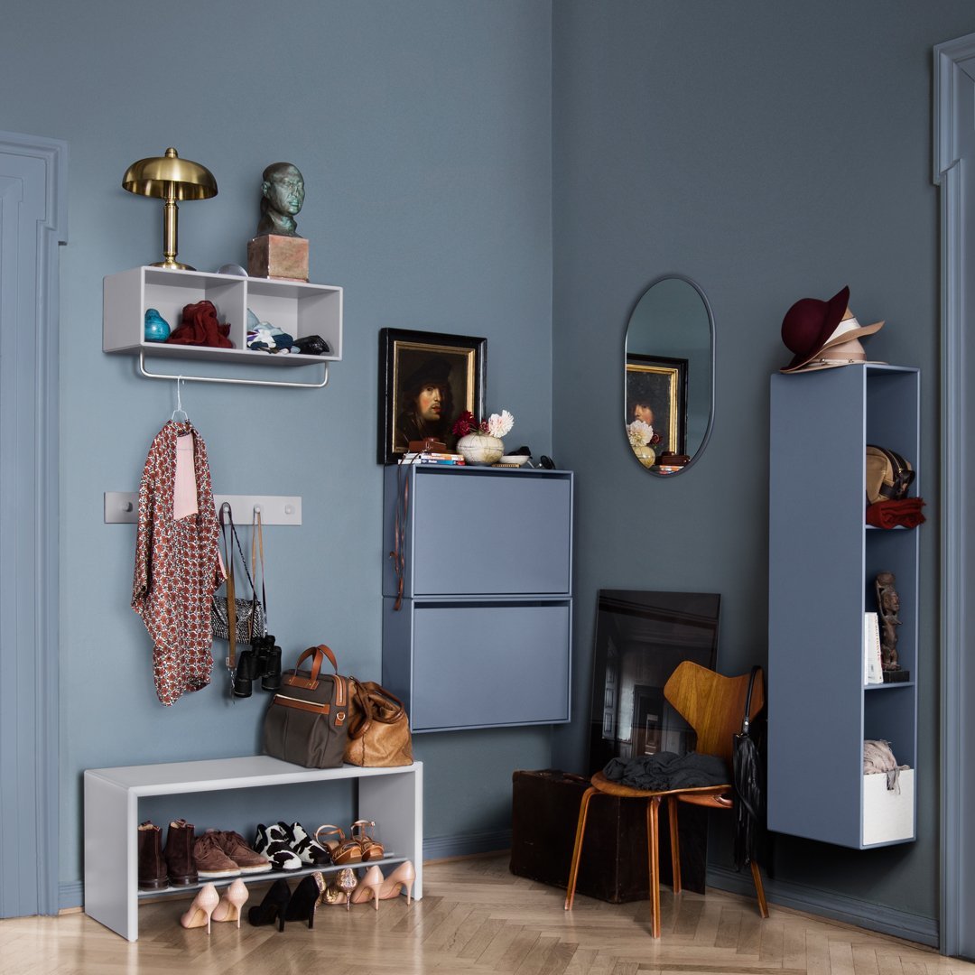 "Blue walls with gray storage units, patterned accessories, and a warm wooden chair create a stylish, modern entryway."