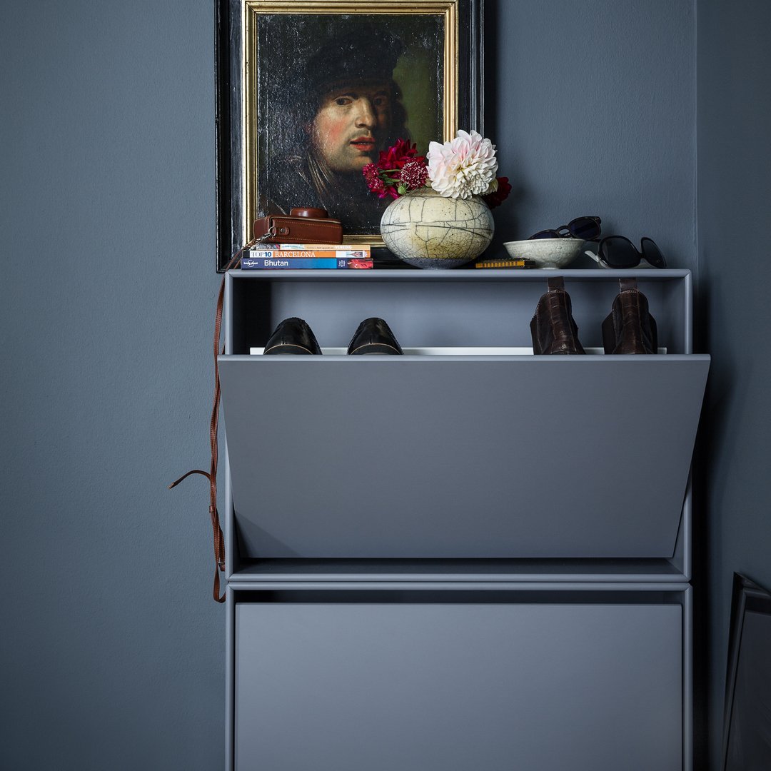 Gray shoe cabinet with sleek design, displayed against a deep blue wall featuring vibrant floral accents and decorative items.