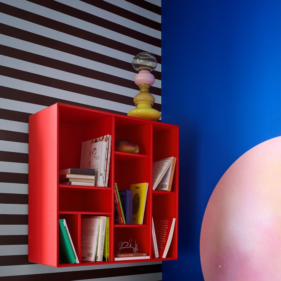 Red floating bookshelf against a striped brown and beige wall, with vibrant blue and pink accents enhancing the scene.