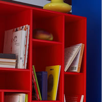 Bright red bookshelf with varied colored books and a bold, yellow vase, set against a blue wall.