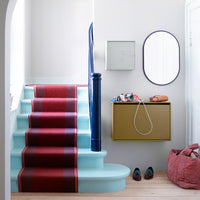 "Soft blue staircase with a red and navy striped runner, gold storage box, and burgundy basket accents."