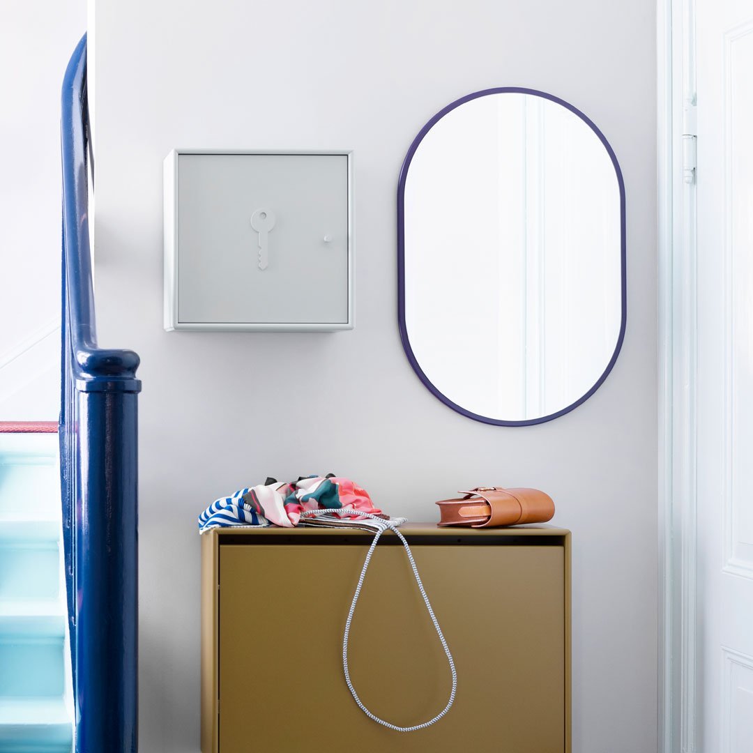 Gray key box and purple-framed mirror above a smooth gold cabinet, with colorful patterned items atop. 