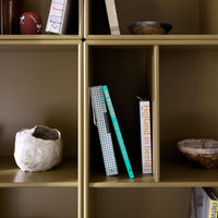 Gold shelving unit with white and turquoise books, a cream ceramic vase, and dark patterned bowls.