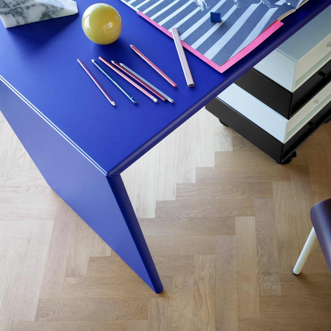 Vibrant purple desk with colorful pencils and striped paper on a light wooden floor, adding a playful touch to decor.